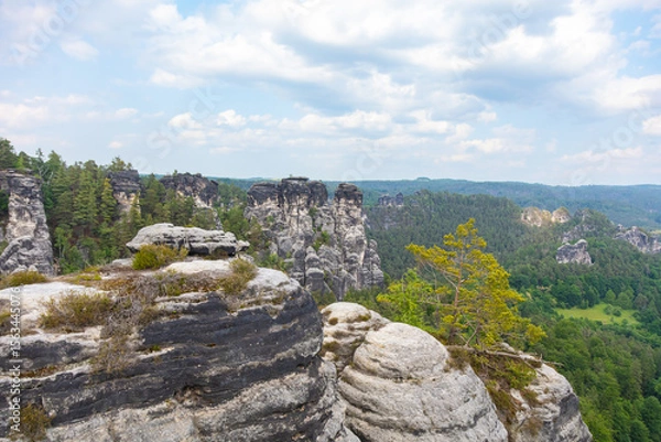 Obraz Bastei, Germany - June 3rd, 2025: Tourists walk along the historic Bastei Bridge in Saxon Switzerland National Park, Germany, surrounded by dramatic sandstone rocks and lush greenery on summer day