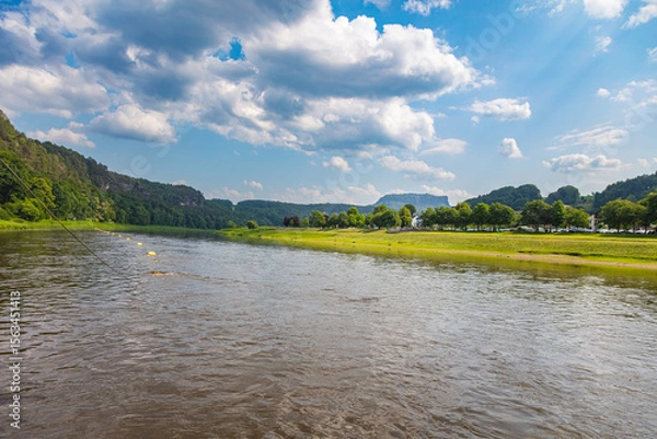 Obraz Scenic summer view of the Elbe River at Rathen, Saxon Switzerland. near the Bastei. Traditional houses, forested sandstone cliffs, and low water levels define this peaceful German river landscape.