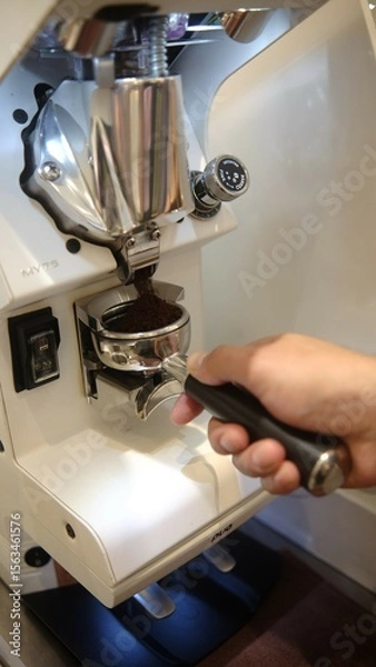 Fototapeta person barista using modern grinder machine to prepare coffee grounds in cafe features digital display and  polished metal finish.  