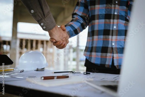 Fototapeta Two builders shaking hands at a construction site, representing a successful agreement and partnership built on trust, cooperation, and a shared goal of developing and growing real estate.