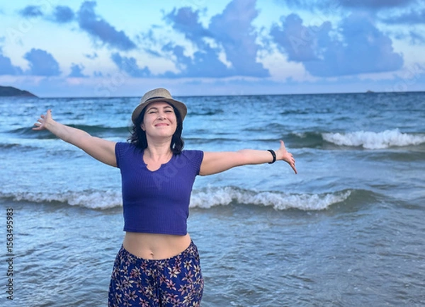 Fototapeta A joyful woman standing by the ocean with open arms, embracing nature and freedom, happy woman enjoying freedom at the sea with arms wide open, horizontal shot