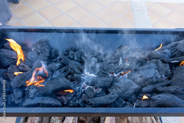 Fototapeta Burning charcoal embers creating smoke and flames in a barbecue grill
