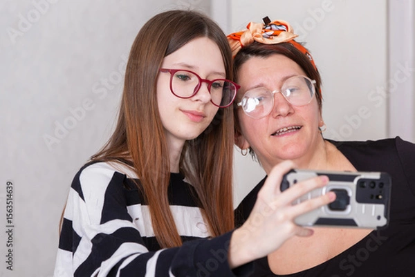 Obraz Two women take a selfie together indoors while enjoying a moment of connection and laughter in a cozy setting