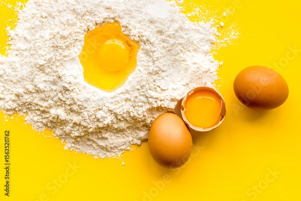 Obraz Making dough concept. Pile of flour and eggs on yellow background top view