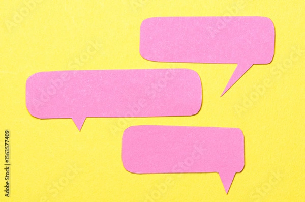 Fototapeta Pink blank cut out paper speech bubbles with copy space for text on yellow background, flat lay top view conceptual conversation backdrop