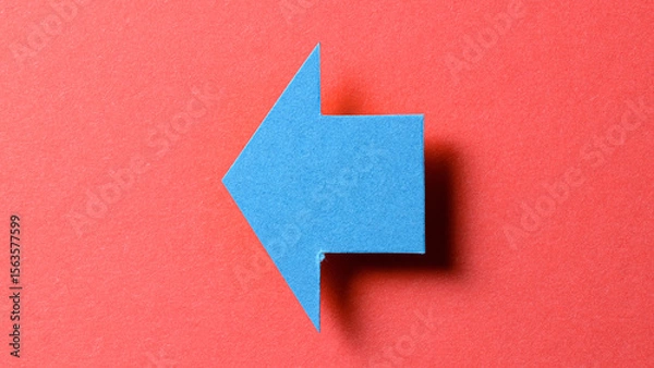 Fototapeta Blue blank paper cardboard arrow direction sign with shadow and copy space for text on red background, flat lay top view pointing symbol message backdrop