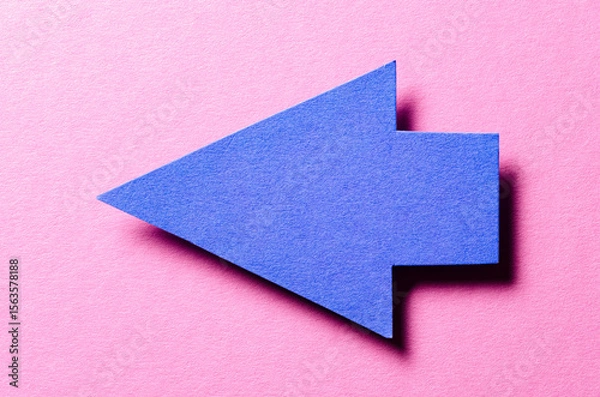 Fototapeta Blue cut out blank paper cardboard arrow direction sign with copy space for text on pink background, flat lay top view pointing symbol conceptual message backdrop