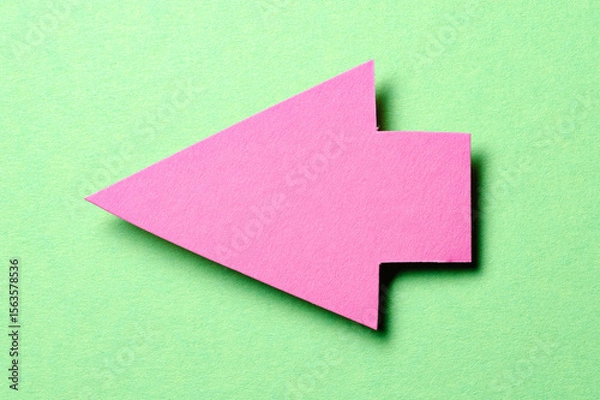 Fototapeta Pink cut out blank paper cardboard arrow direction sign with copy space for text on green background, flat lay top view pointing symbol conceptual message backdrop