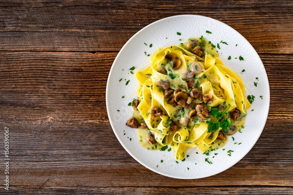 Fototapeta Papperdelle pasta with champignons mushrooms in cream sauce and parsley on wooden table