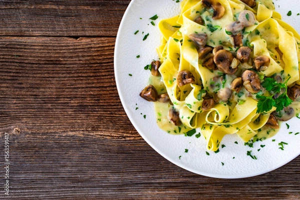Fototapeta Papperdelle pasta with champignons mushrooms in cream sauce and parsley on wooden table
