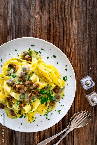 Fototapeta Papperdelle pasta with champignons mushrooms in cream sauce and parsley on wooden table