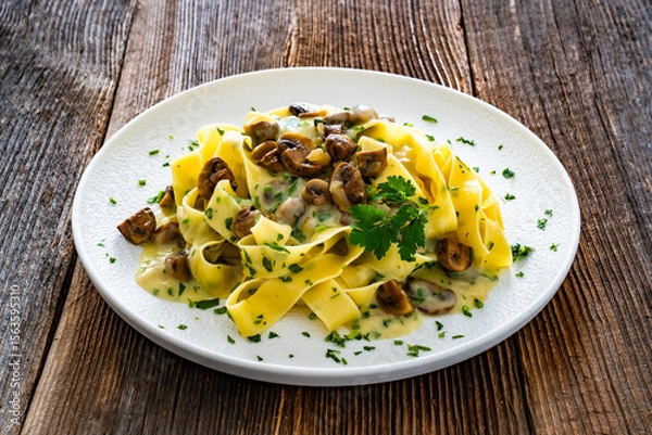 Fototapeta Papperdelle pasta with champignons mushrooms in cream sauce and parsley on wooden table
