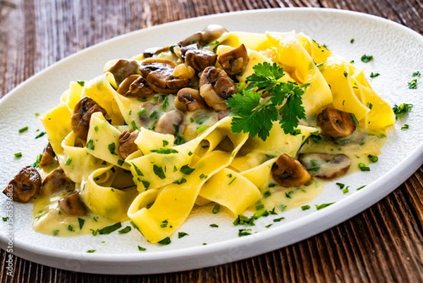 Fototapeta Papperdelle pasta with champignons mushrooms in cream sauce and parsley on wooden table