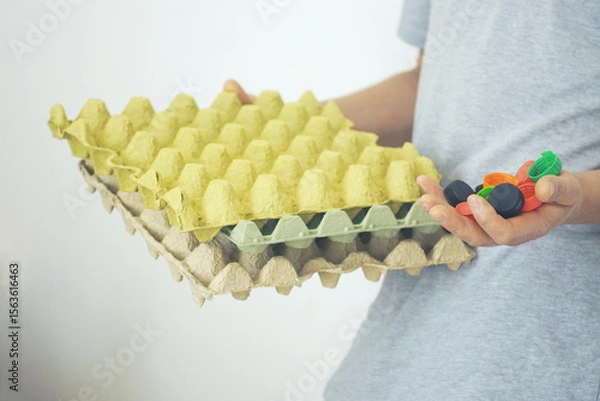 Fototapeta Practical eco-living choices. A man holds a collection of plastic lids and paper packaging, symbolizing minimal waste mindset and daily commitment to preserving nature and fighting plastic pollution