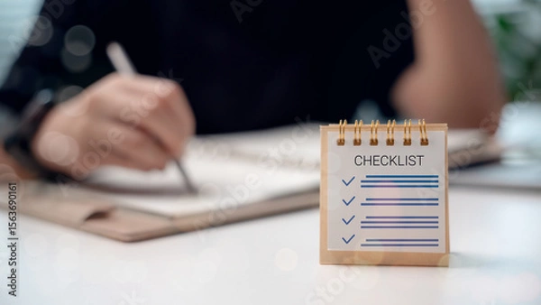 Obraz Close-up of a checklist on a desk with a businessman writing in a notebook, representing planning, productivity, and task management.