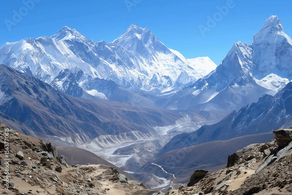 Fototapeta a mountain range with a river running through it and snow capped mountains in the background, with a blue sky