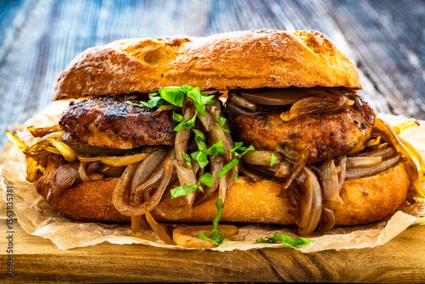 Fototapeta Takeaway sandwich with fried minced cutlets and caramelized onion on wooden table