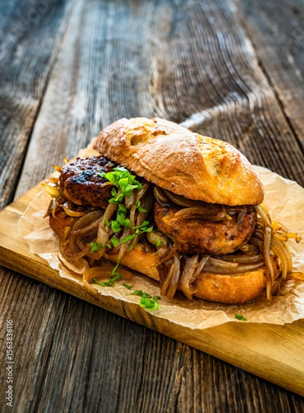 Fototapeta Takeaway sandwich with fried minced cutlets and caramelized onion on wooden table