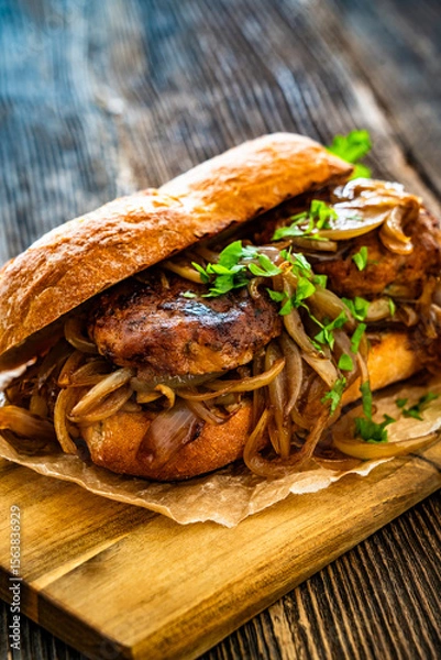 Fototapeta Takeaway sandwich with fried minced cutlets and caramelized onion on wooden table