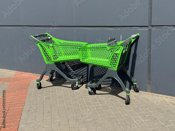 Obraz Two bright green shopping carts parked near a dark gray wall outside a store. Urban detail with contrast in colors