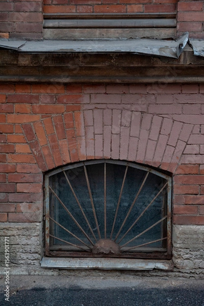 Obraz Rusty iron bars cover an arched basement window set in aged brick