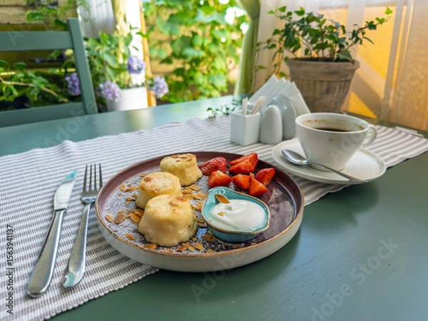 Obraz Gourmet breakfast served outdoors: A plate of syrniki with fresh strawberries on a green wooden table.