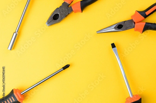 Fototapeta Empty yellow background with flathead philips screwdriver and pliers sides top view