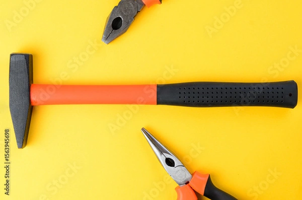 Fototapeta Hammer centered with cropped pliers on both sides on bright yellow background top view