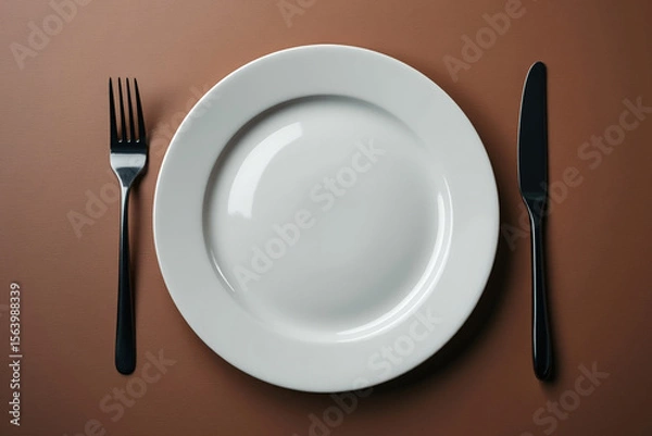 Fototapeta Minimalist Table Setting with White Plate Black Fork and Knife on a Brown Surface A Clean and Modern Dining Arrangement