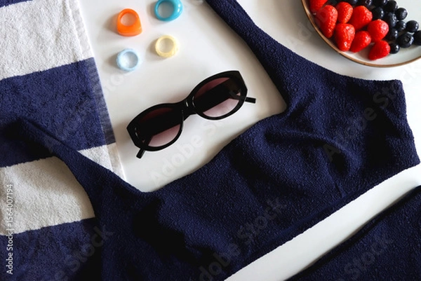 Obraz Navy swimsuit, striped beach towel, sunglasses, colorful rings and plate with berries. Top view.