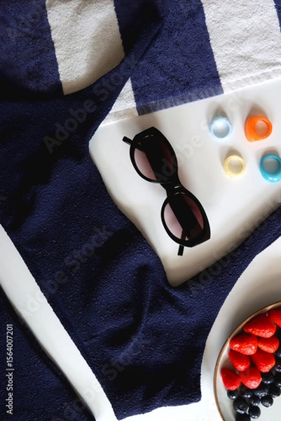 Obraz Navy swimsuit, striped beach towel, sunglasses, colorful rings and plate with berries. Top view.