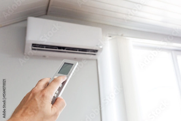 Fototapeta A man holds an air conditioner remote control in his hand. A man turns on the air conditioner. Unbearable heat.