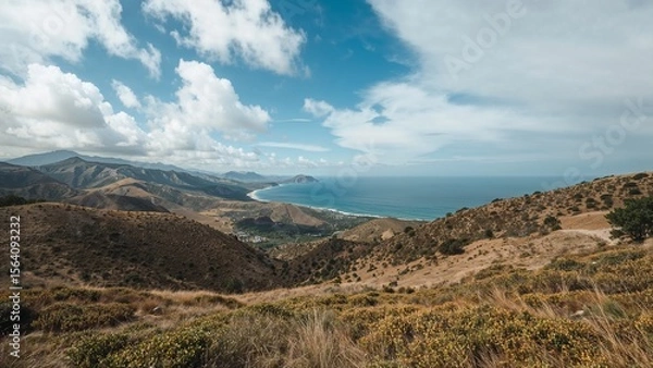 Fototapeta Verdant hillsides meet azure seas under a vast, bright sky in a coastal vista, presenting a scene of nature's beauty and tranquility.