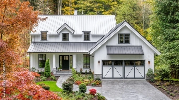 Obraz White farmhouse with a gray roof and wide front windows. Features a central entrance and garage, framed by colorful, manicured plants.