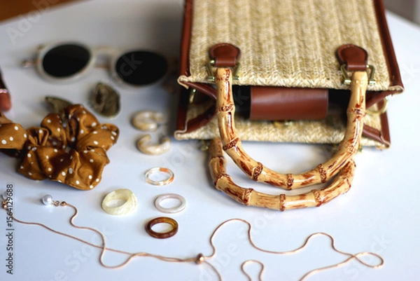 Obraz Wicker purse, sunglasses, scrunchie, lipstick and various gold and neutral jewelry on white background. Selective focus.