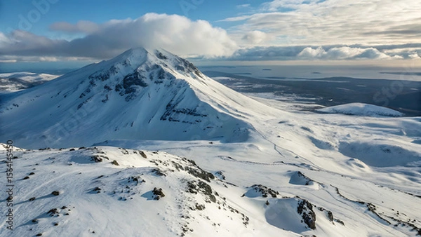 Fototapeta Snowy mountain peak under a cloudy sky with a view of the distant ocean and landmasses beyond - ai generated