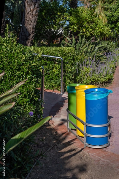 Fototapeta Colorful recycling bins in lush garden setting