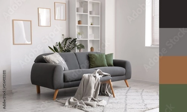 Fototapeta Grey sofa with cushions and plaid, shelving unit and frames on white wall in living room. Different color patterns