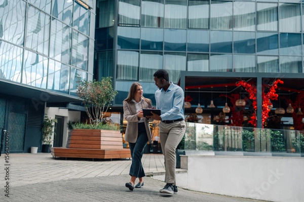 Fototapeta Businesspeople walking and talking, using tablet in urban setting