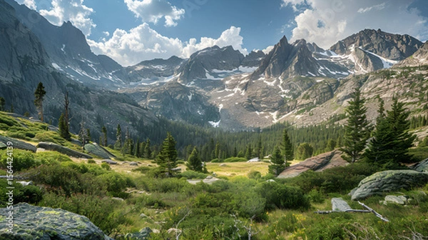 Fototapeta Valley view with rocky mountains snowy peaks and evergreen trees under a partly cloudy sky day light
