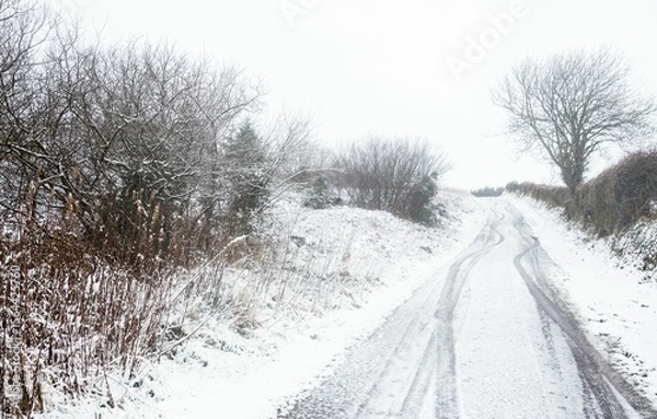 Fototapeta Flat design is showing winding snow-covered lane curving uphill with twin tracks and hedgerows