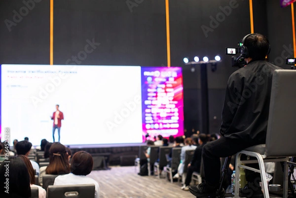 Fototapeta selective focus to cameraman with blurry video camera set are recording to speaker and audience in conference hall or seminar event. exhibition convention center.