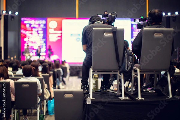 Fototapeta selective focus to cameraman with blurry video camera set are recording to speaker and audience in conference hall or seminar event. exhibition convention center.