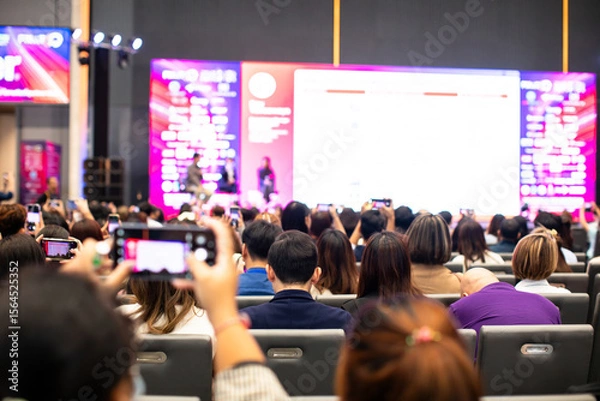 Fototapeta Selective focus to audience with blurry the cameraman and video camera set to recording the speaker and audience in conference hall or seminar event. exhibition convention center.