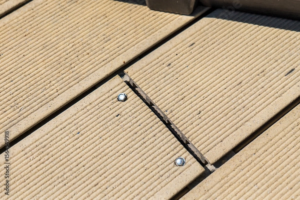 Fototapeta Damaged composite decking boards with visible cracks due to poor installation. Close-up of light brown planks with metal screws and misaligned joints.