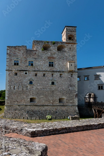 Fototapeta Stone tower of Sárospatak Castle in Hungary with small windows, medieval walls, and wooden bridge, under clear blue sky.
