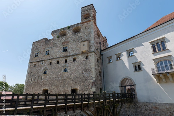 Fototapeta Stone castle tower and white building with wooden bridge in Sarospatak, Hungary, under clear blue sky.