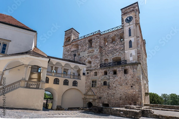 Fototapeta Sarospatak castle courtyard with historic stone tower and clock, arched gallery, and cobblestone path under clear blue sky in Hungary.