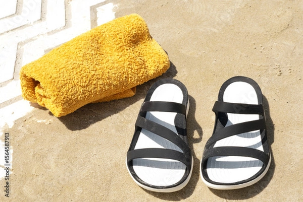 Obraz Black sandals and a yellow towel resting on sandy beach during a sunny day