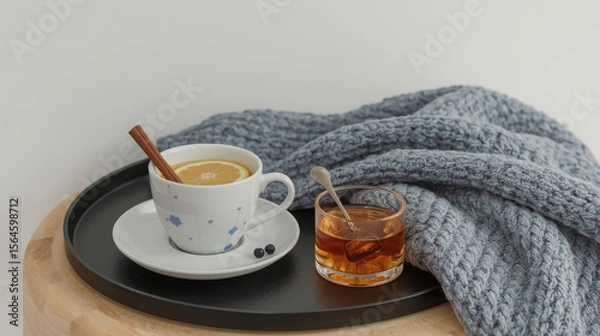Fototapeta Cozy composition with a hot drink with lemon and cinnamon, a glass of whiskey, and a blue knitted blanket.
